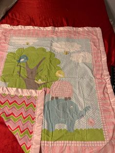 a pink blanket with an elephant, giraffe and tree design on it next to a red bedspread