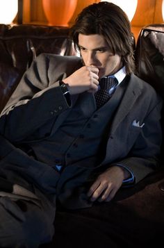 a man in a suit and tie sitting on a couch with his hand under his chin