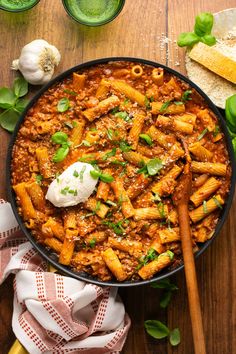 a skillet filled with pasta and sauce on top of a wooden table next to garlic