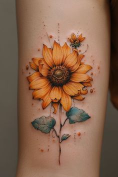 a yellow sunflower tattoo on the side of a woman's thigh with leaves