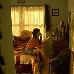 a woman sitting on top of a bed next to a window