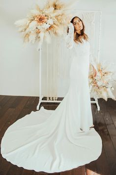 a woman standing in front of a white backdrop with flowers and feathers on her head