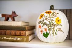 a painted pumpkin sitting on top of a white shelf next to books and a wooden star