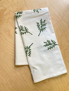 two napkins with green leaves on them sitting on a wooden table top next to each other