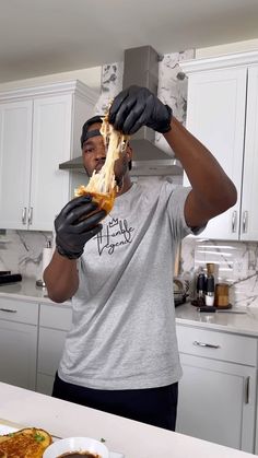 a man in black gloves holding up a piece of food to his face with both hands