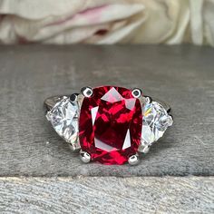 a close up of a ring with a red stone in the middle and three diamonds around it