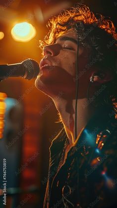 a young man singing into a microphone in front of a bright light at an event