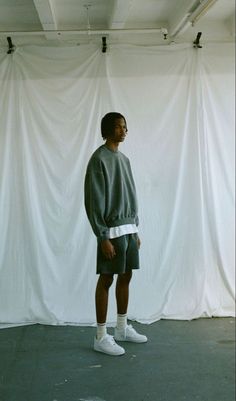 a young man standing in front of a white backdrop wearing shorts and a grey sweatshirt