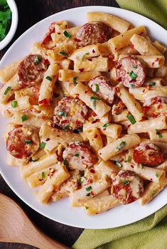 a white plate topped with pasta covered in sausage and tomato sauce next to a bowl of parsley