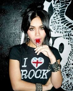 a woman with black hair holding a red lip in front of her face and wearing an i love rock t - shirt