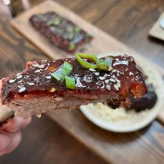 a person holding up a piece of meat with sauce and green peppers