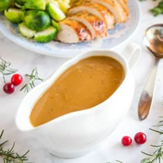 a bowl of gravy next to a plate of meat and vegetables