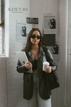 a woman in black jacket and sunglasses holding a tablet next to a wall with posters on it