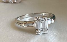 NOTE: THIS AUCTION IS ONLY FOR THE VINTAGE 1950S EMERALD CUT DIAMOND RING with BAGUETTES - 14K WHITE GOLD. All other items: are Strictly For Display. Blue Ring Box IS NOT INCLUDED. Item will come in another presentation box. This gorgeous ring is set with ONE CENTER SPARKLY EMERALD CUT DIAMOND approximately .40 carats and enhanced by 2 SMALL BAGUETTE DIAMONDS SET ON EACH SIDE. The Ring Size is approximately 6 and can be re-sized.  This elegant piece would look nice in a stack or paired with a ring of similar style or era (as shown in the photos). It would also make a beautiful engagement ring! Note: SOLD AS IS. This item is vintage so it does show signs of wear typical for its age. Please refer to the pictures (PHOTOS TAKEN IN NATURAL DAYLIGHT) as they are part of the description. Kindly e Art Deco Engagement Ring White Gold, Platinum Vintage Engagement Rings, Vintage Engagement Rings Unique 1920s Silver, Wedding Rings Silver Vintage, Emerald Cut Platinum Engagement Ring, Emerald Engagement Ring With Baguettes, Emerald Cut Stack, Bezel Engagement Ring Silver, Engagement Rings Silver Vintage