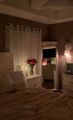 a bed room with a neatly made bed next to a window and a vase filled with flowers