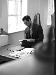 a man sitting at a desk in front of a lamp and looking through a book