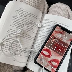 an open book with earbuds laying on top of it next to a cell phone