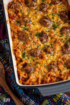 a casserole dish with meatballs and cheese in it on a colorful cloth