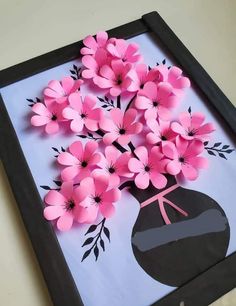 pink paper flowers in a black vase on a white tablecloth with a blue background