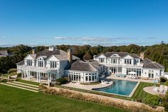 an aerial view of a large white house with a pool in the foreground and lots of greenery surrounding it