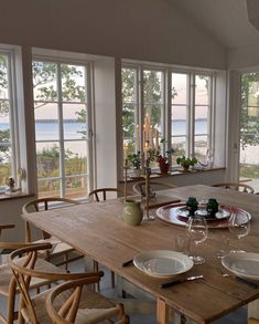 a wooden table with plates and glasses on it in front of large windows overlooking the water