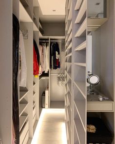 an empty walk - in closet with white shelves and drawers on both sides is lit by recessed lighting