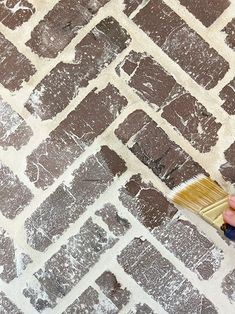 a person is using a brush to paint a brick wall with white and brown colors