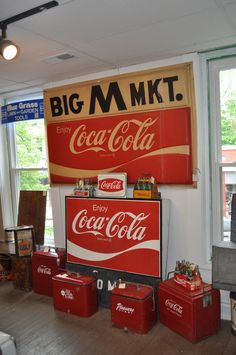 an old coca - cola advertisement hangs on the wall next to other vintage coke cans