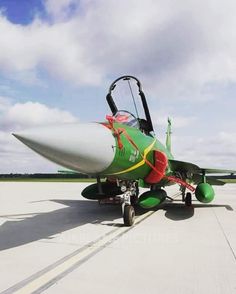 a green and red fighter jet sitting on top of an airport tarmac