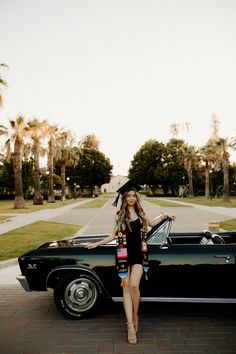 a woman standing next to a black car in front of palm trees and a street