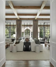 an open living room with white furniture and wood beams on the ceiling, along with large windows