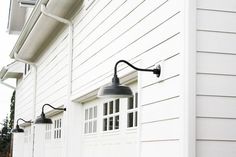 two black lamps on the side of a white building with windows and shutters in front of it