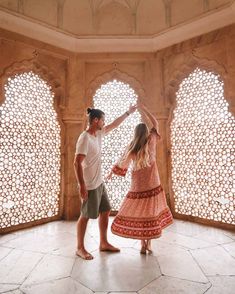 a man and woman standing in front of an ornate wall with arched windows, dancing