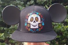 "Coco Hat. Mickey Ears. Pixar Coco Hat. Mouse Ears. \"Remember me\" We created this beautiful custom Coco Hat with a black flat bill snap back cap, authentic black ears and vinyl cut outs in the fiesta flags from the movie.  The custom embroidered patch  is so cute and colorful.  We finished the look with an orange flower petal  mickey on the back. Please allow 2 weeks to create." Pixar Coco, Snap Back Cap, Custom Embroidered Patches, Remember Me, Vinyl Cut, Flower Petal, Orange Flower, Mickey Ears, Snap Back