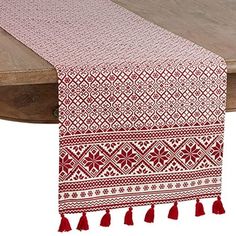 a red and white table runner with tassels on top of a wooden table