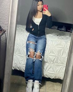 a woman taking a selfie in the mirror with her cell phone and ripped jeans