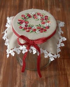 a glass jar with a red ribbon around it on a wooden table next to a doily