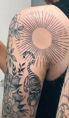 the back of a woman's shoulder with tattoos on it and flowers around her