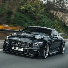 a black car driving down the road with trees in the backgroung area