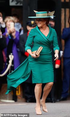 a woman in a green dress and hat is walking down the street while people are taking pictures behind her