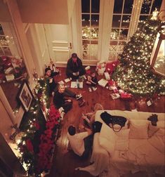 people are sitting on the floor in front of christmas trees with presents all around them