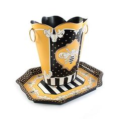 a black and yellow vase sitting on top of a plate next to a tray with a bee design