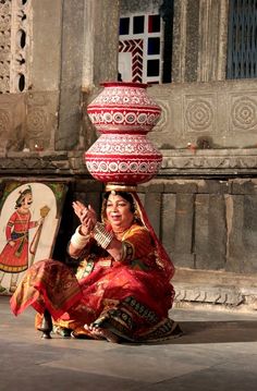 a woman sitting on the ground in front of a building with a large red vase