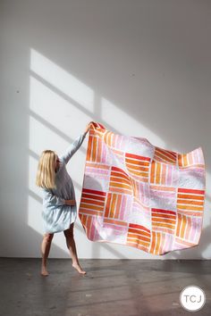 a woman is holding up a quilt in the air with her hands and feet on the ground