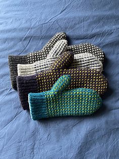 four knitted mittens laying on top of a blue bed sheet with one folded up and the other lying down