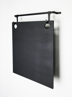 a black piece of art hanging on a white wall with a metal hook attached to it