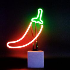 a neon sign that is on top of a white block in front of a black background