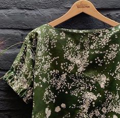 a green shirt with white flowers is hanging on a wooden hanger next to a brick wall