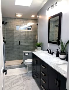 a bathroom with two sinks, a toilet and a walk in shower area that has gray tiles on the walls