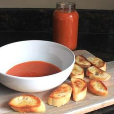 a bowl of tomato soup and some bread on a cutting board